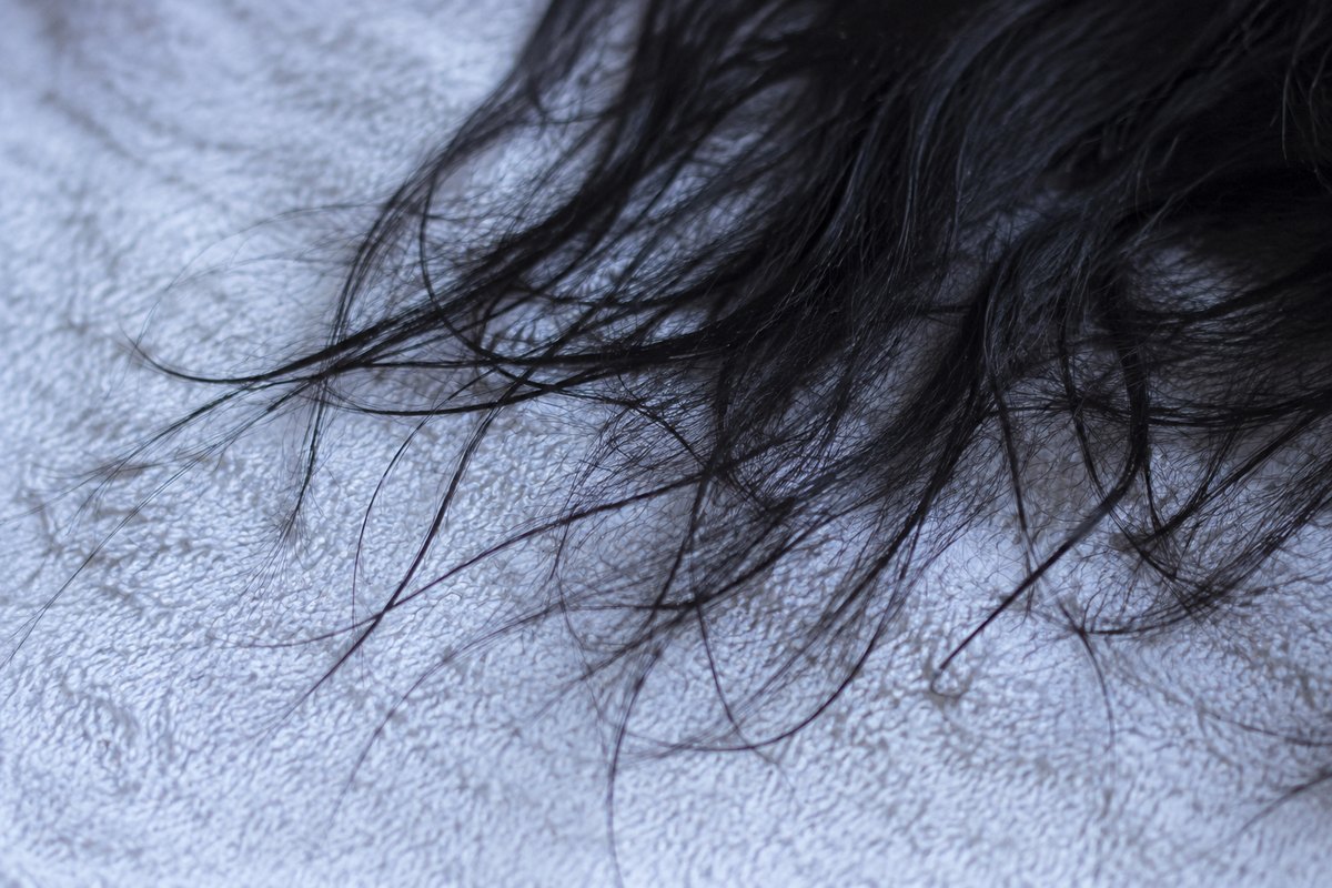 Helai rambut gelap di atas tuala pucat, cahaya sisi, tiada produk